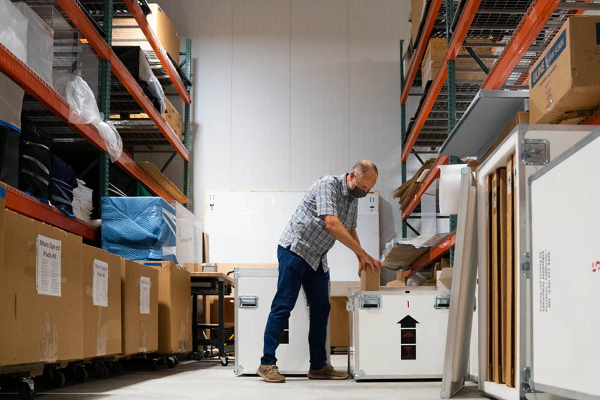 A person is leaning over a crate and placing a box in it